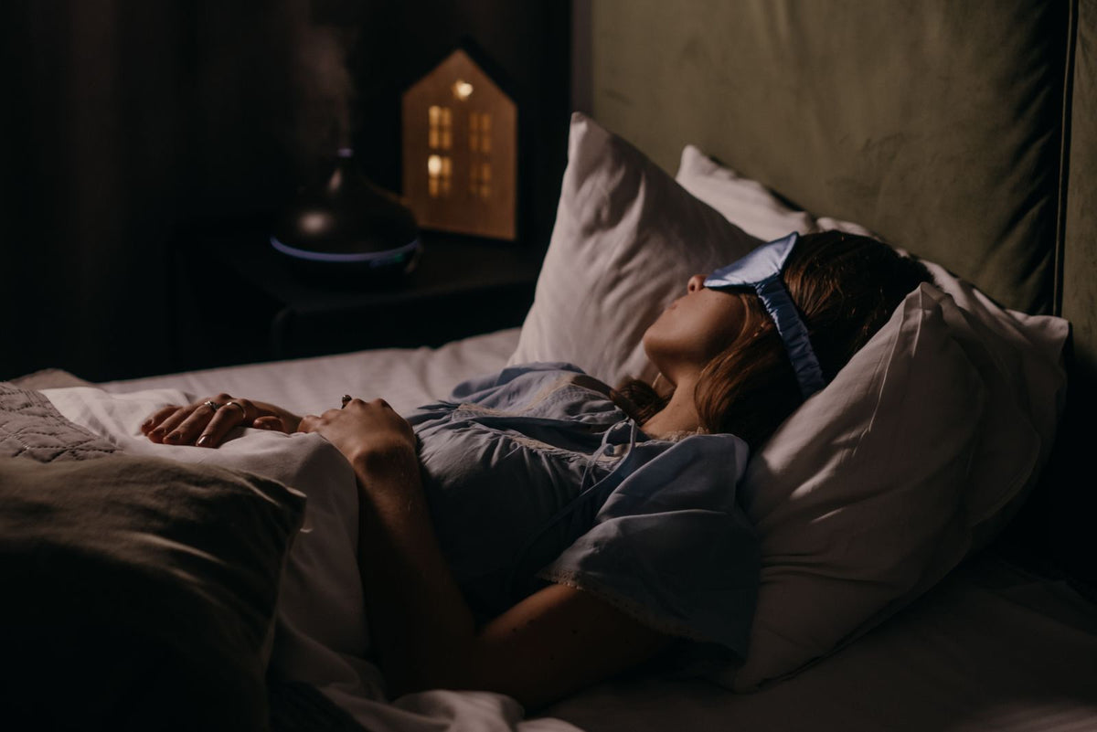 Vrouw slaapt vredig met een oogmasker in een donker verlichte, rustige slaapkamer