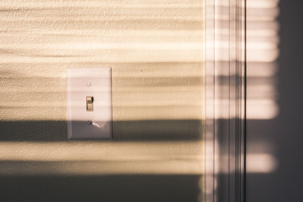 Lichtschakelaar op een muur met schaduwen van gesloten jaloezieën