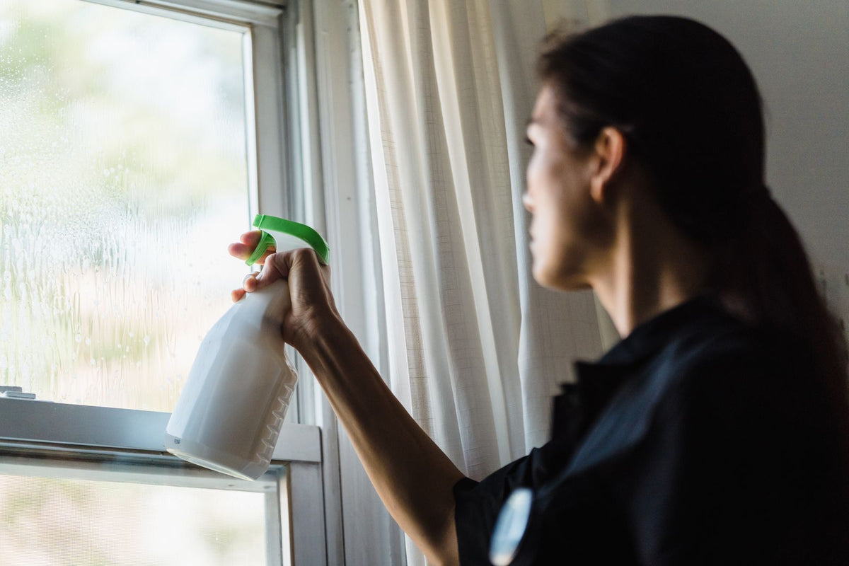 Persoon maakt een raam schoon met een schoonmaakspray